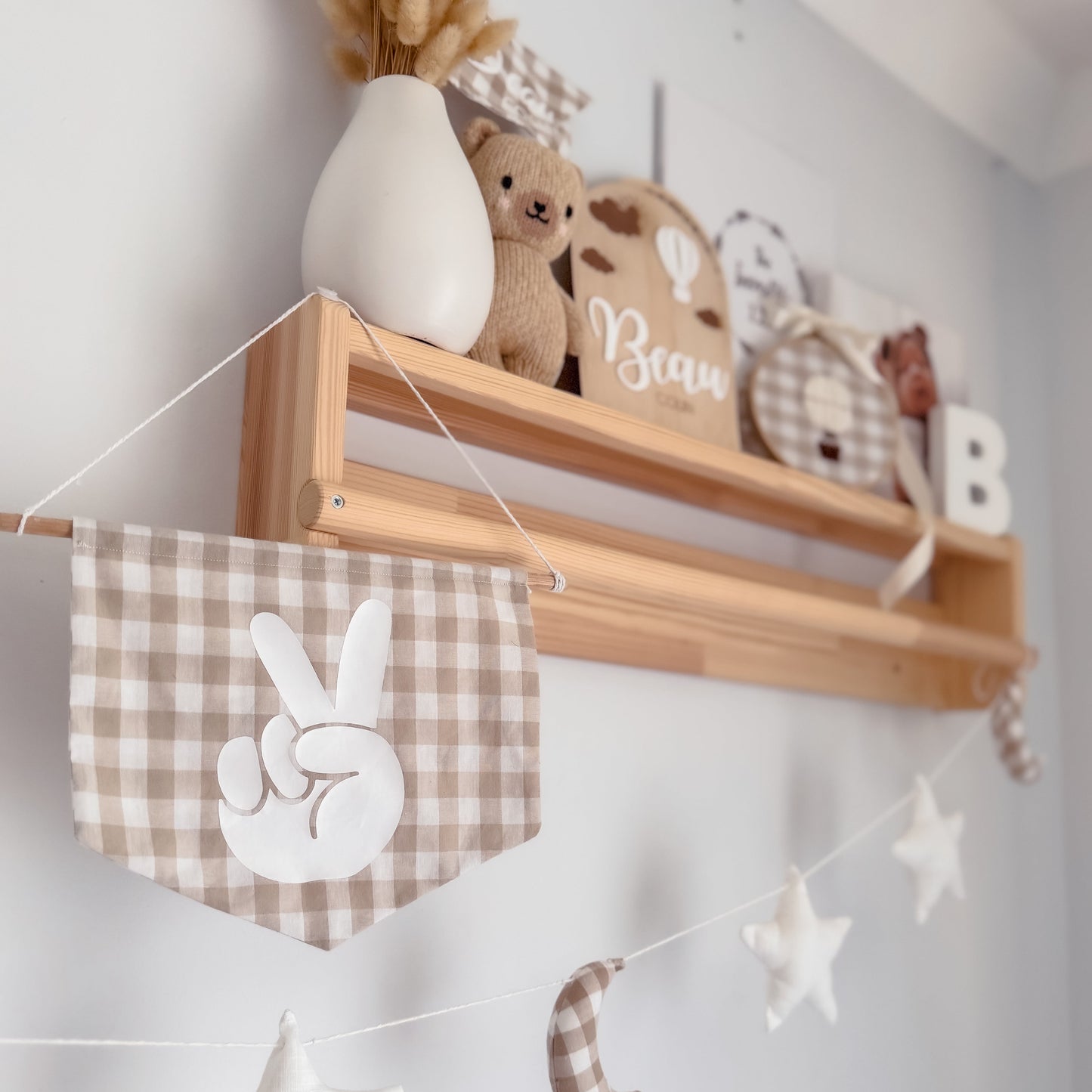 Wooden shelf with decorative items including a teddy bear, a vase, and a banner with peace signs and stars on a white wall.