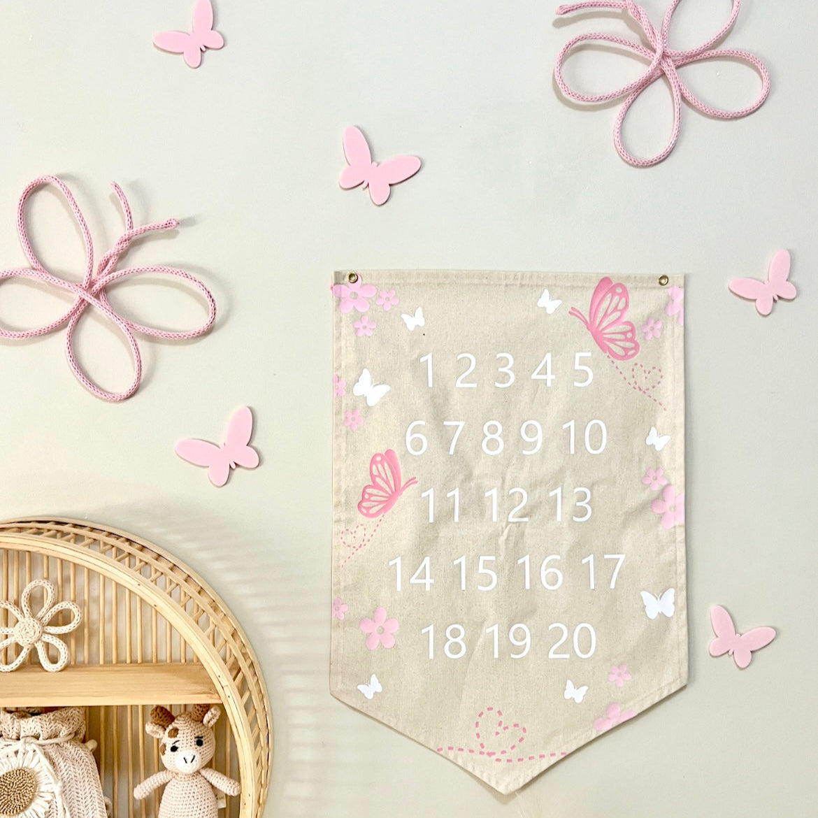 A decorative banner with a butterfly design, displaying numbers 1 to 20, hanging on a wall with more decorative butterflies and a wicker basket with a teddy bear.