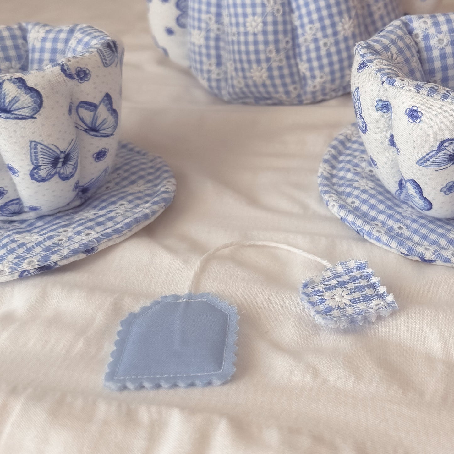 Fabric tea set with teapot, cups, and bowls on a bed