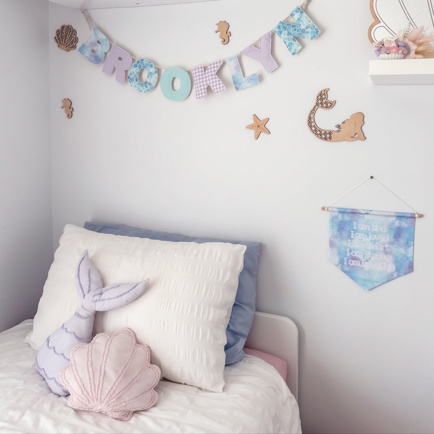 Children's room with decorative mermaid pillows, a name banner, and wall art.