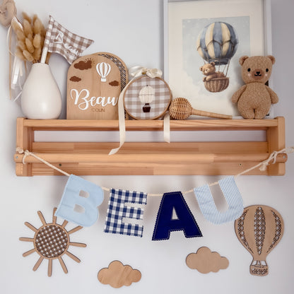 Nursery shelf with decorative items including a teddy bear, wooden letters, and a hot air balloon-themed painting.