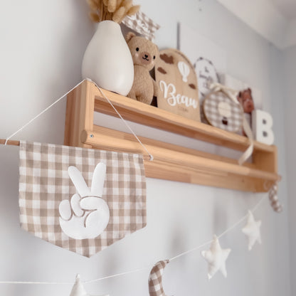 Wooden shelf with decorative items including a teddy bear, a vase, and a banner with peace signs and stars on a white wall.
